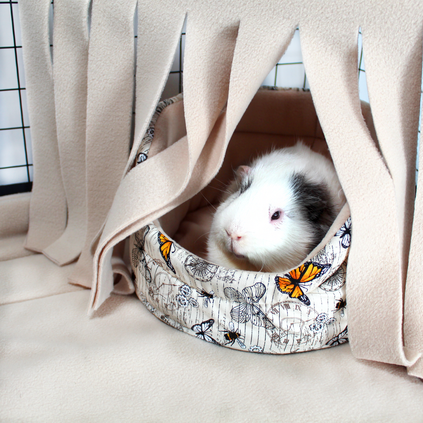 Steampunk Butterfly Cuddle Cup Bed, showing it inside a cage underneath a matching fleece forest with a happy guinea pig relaxing