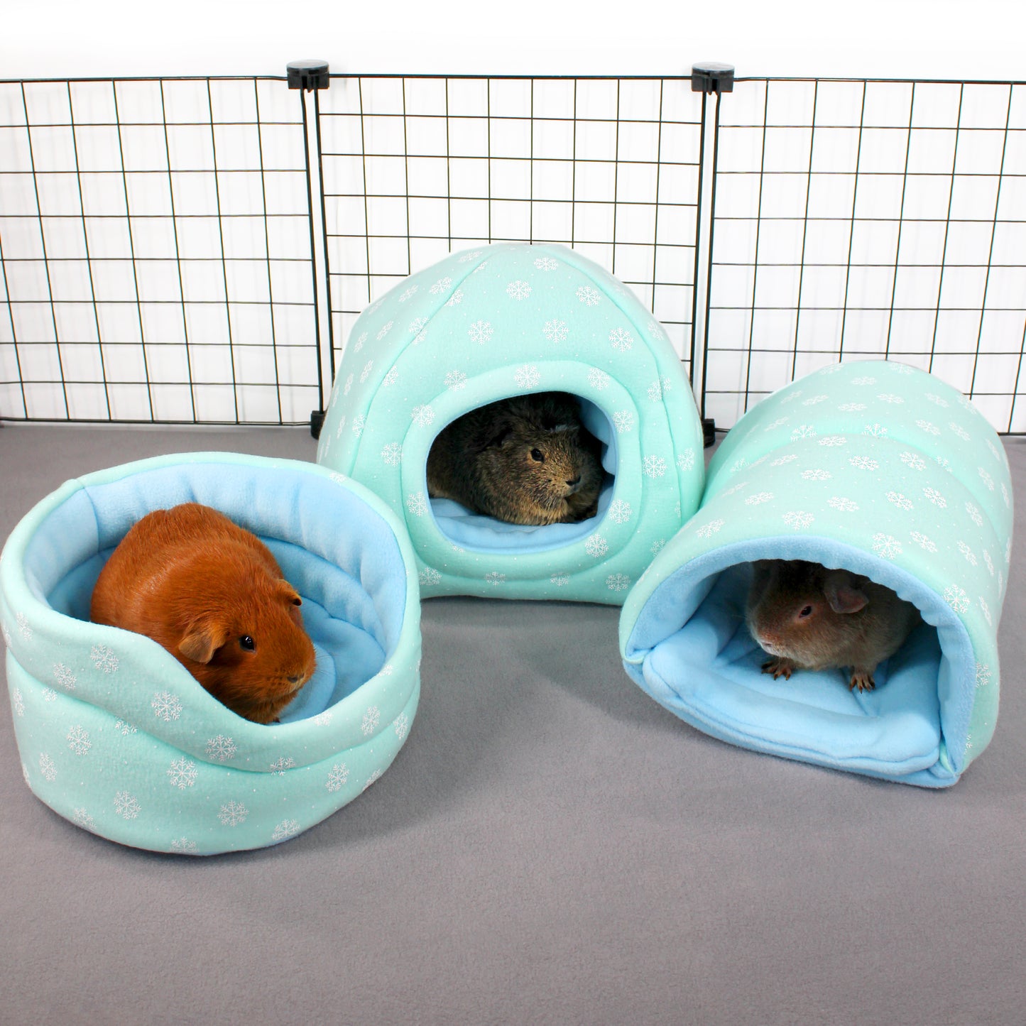 Three small pet houses with guinea pigs inside on a gray surface.
