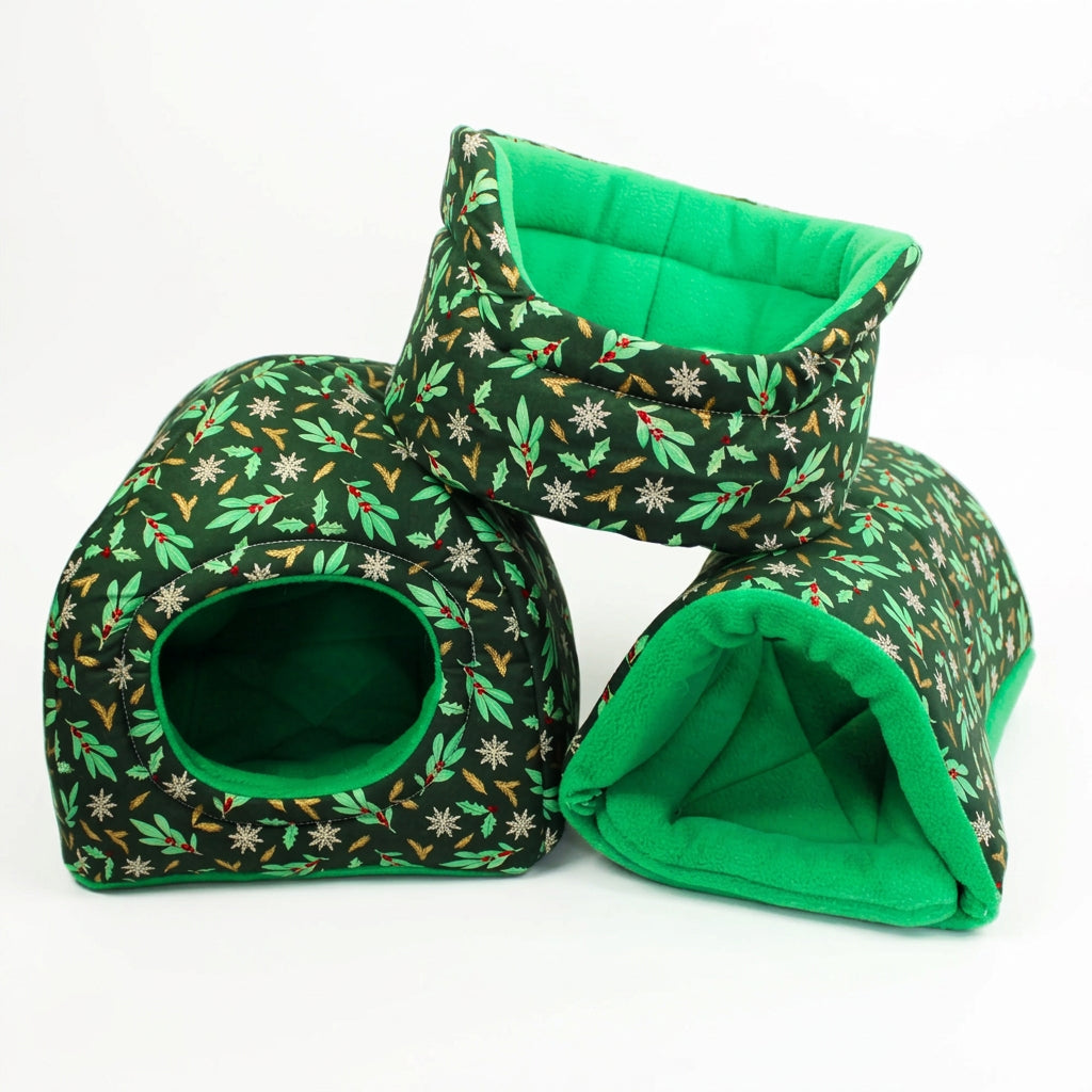 Festive Holly guinea pig accessory bundle featuring a matching cuddle cup, hidey house and snuggle tunnel in forest green Christmas cotton with holly, red berries, white snowflakes and golden foliage, paired with emerald green fleece lining.