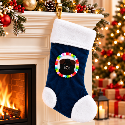 Handmade black guinea pig Christmas stocking with brown ears hanging beside a festive fireplace, featuring a colourful pom-pom border, soft white fleece trim and gold rope hanging loop.