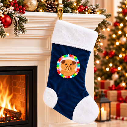 Orange guinea pig Christmas stocking with brown ears hanging beside a decorated Christmas fireplace, featuring a handmade felt guinea pig character, navy blue velvet, fluffy white trim, colourful pom-poms and gold rope hanging loop.