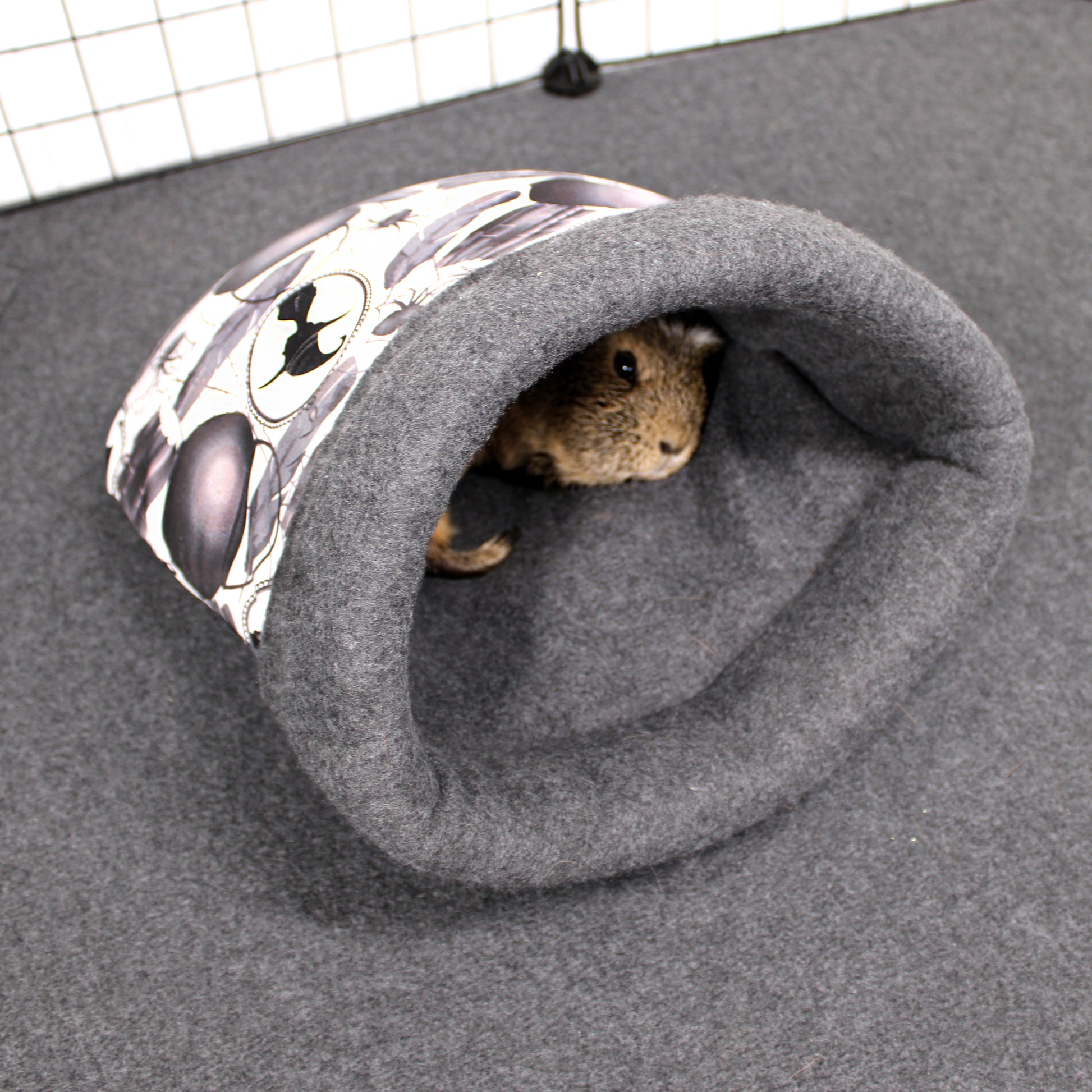 Small animal peeking out from a gray cuddle sack with a patterned entrance on a gray surface.