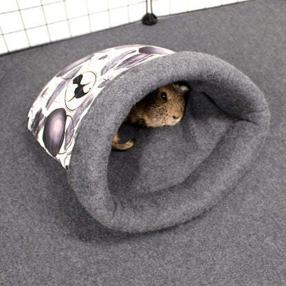 Small animal peeking out from a gray cuddle sack with a patterned entrance on a gray surface.