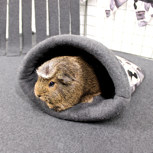 Guinea pig peeking out from a gray pet cave on a gray floor.