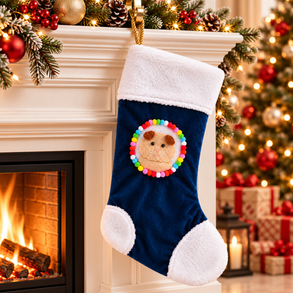 Fluffy cream and ginger guinea pig Christmas stocking hanging beside a decorated Christmas fireplace, with brown ears, colourful pom-poms, white fleece trim and a gold rope hanging loop.