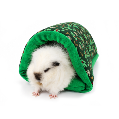 White guinea pig relaxing inside a festive green snuggle tunnel decorated with holly leaves, red berries, white snowflakes and golden foliage