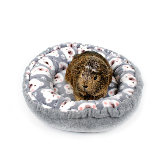 Small animal, likely a guinea pig, in a gray donut bed with white paw prints on a white background