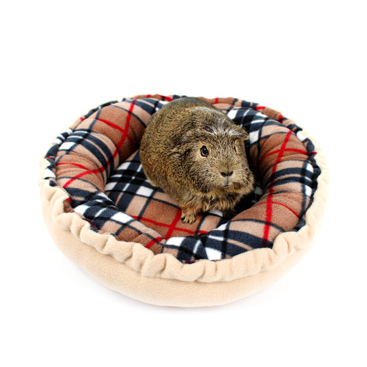 Small animal, likely a guinea pig, sitting on a plaid pet bed with a white background
