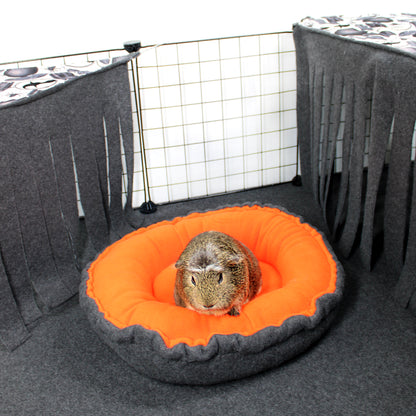 Small animal on an orange and gray pet bed inside a pet enclosure.