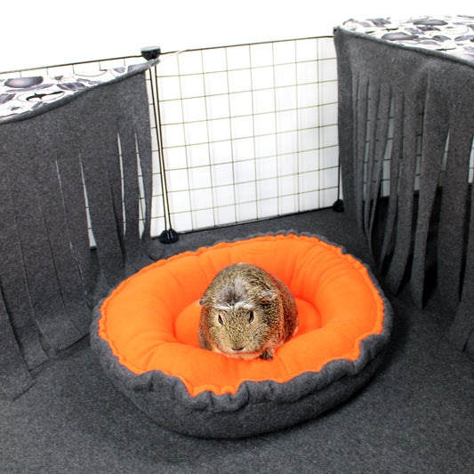 Small animal on an orange and gray pet bed inside a pet enclosure.