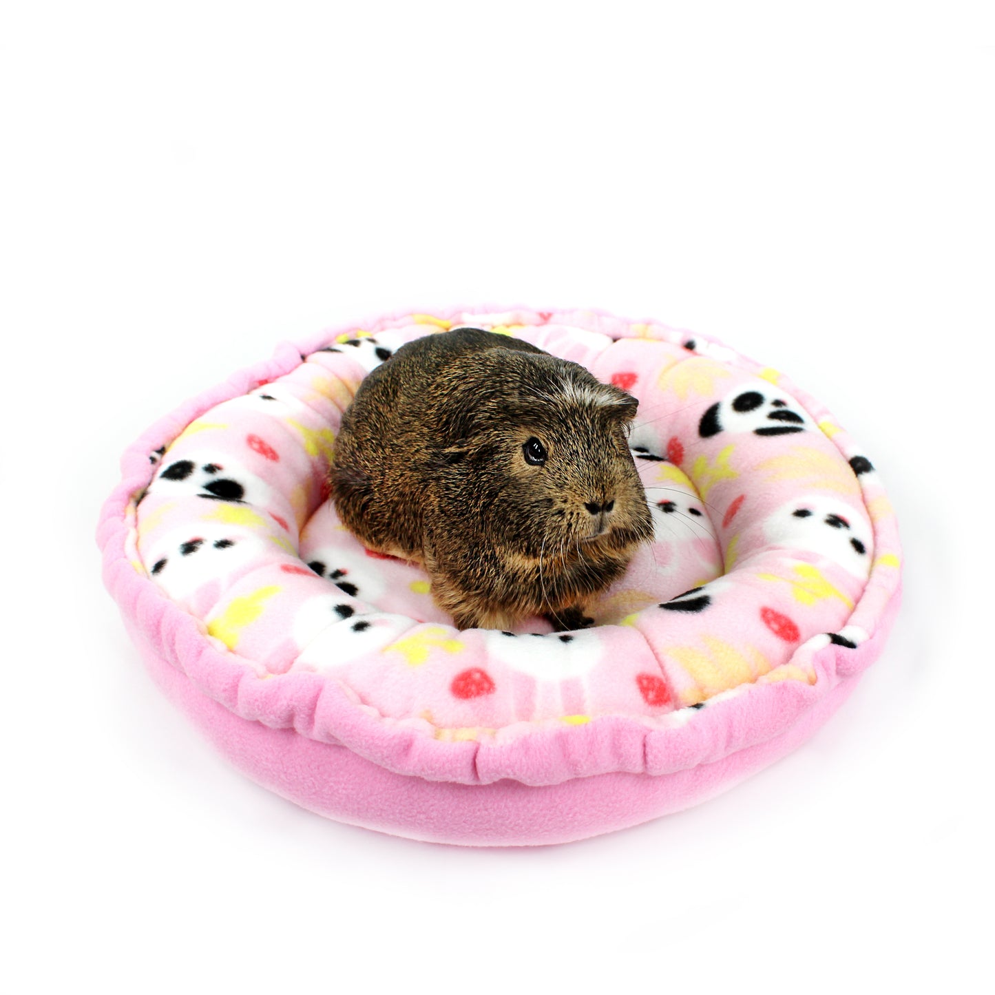 Small animal, likely a guinea pig, sitting on a pink cushion with a donut pattern on a white background