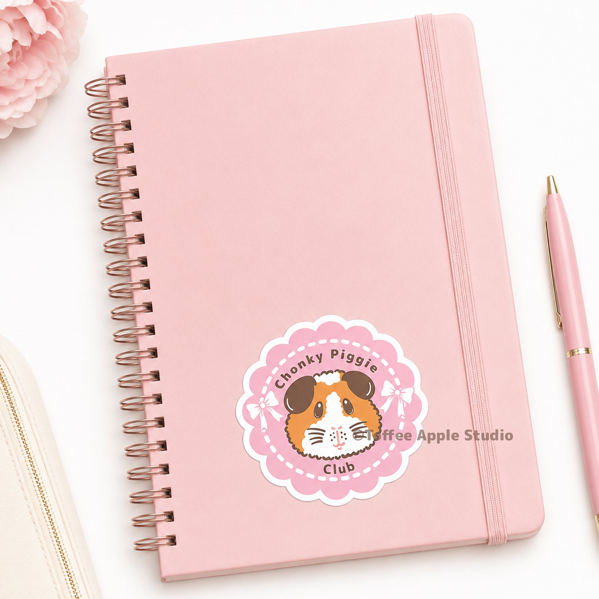 Pink notebook with a sticker featuring a guinea pig and text, on a white background.