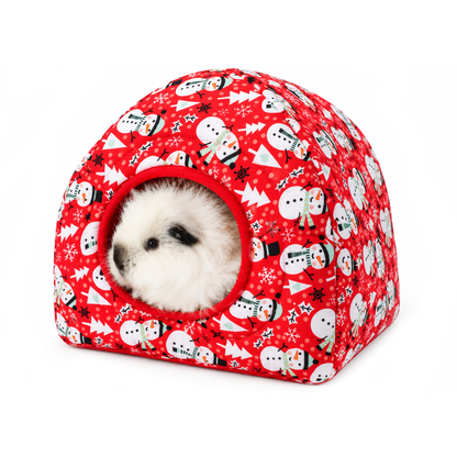 Fluffy white guinea pig sitting inside a red snowman print Christmas hidey house with a soft red fleece-lined entrance