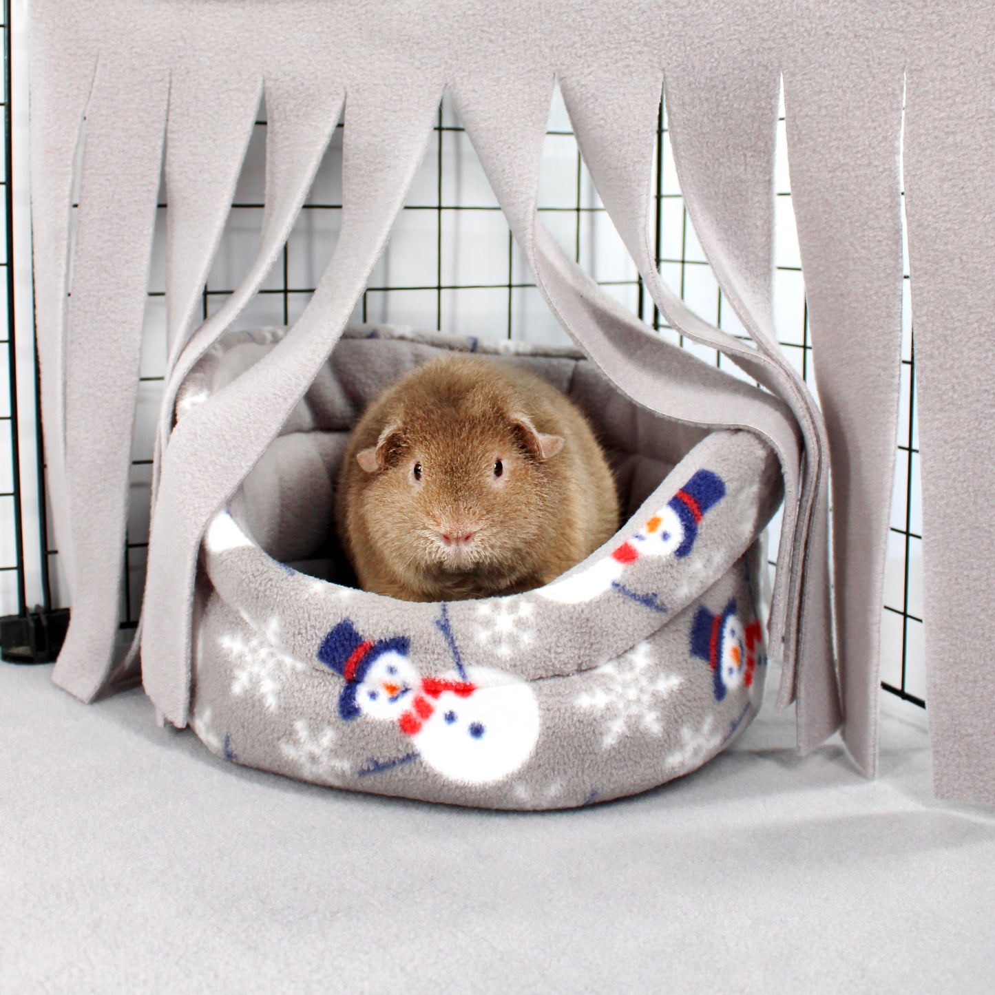 Guinea pig inside a cozy gray pet bed with snowman design on a light background