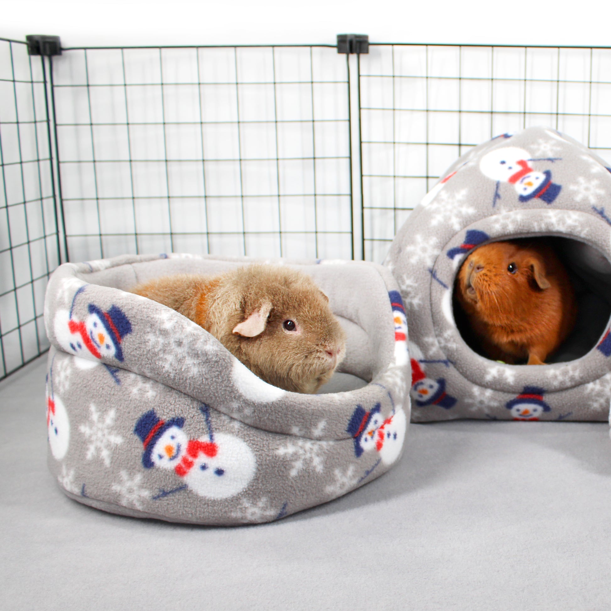 Two guinea pigs in snowman-patterned pet beds inside a wire cage.