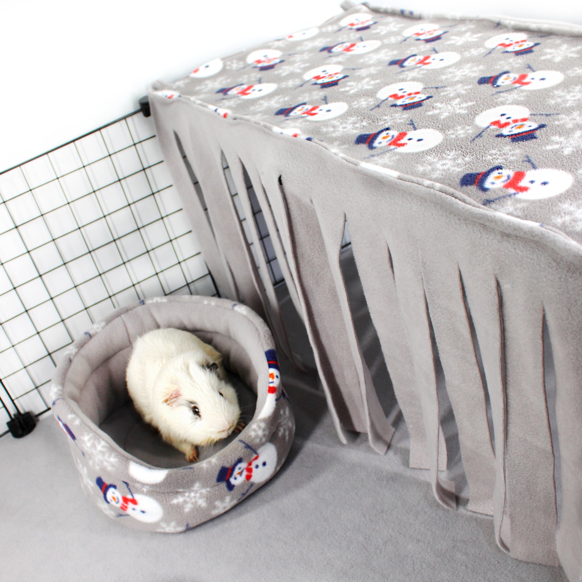 Small animal bed with a snowman pattern next to a gray pet carrier with a white animal inside.