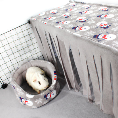Small animal bed with a snowman pattern next to a gray pet carrier with a white animal inside.