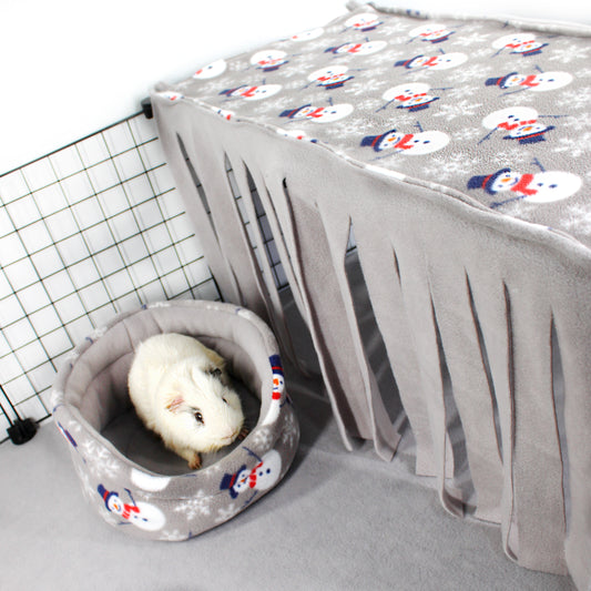 Small animal bed with a snowman pattern next to a gray pet carrier with a white animal inside.